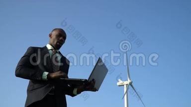 一个穿着商务服的体贴的黑人在风力发电机附近打开笔记本电脑